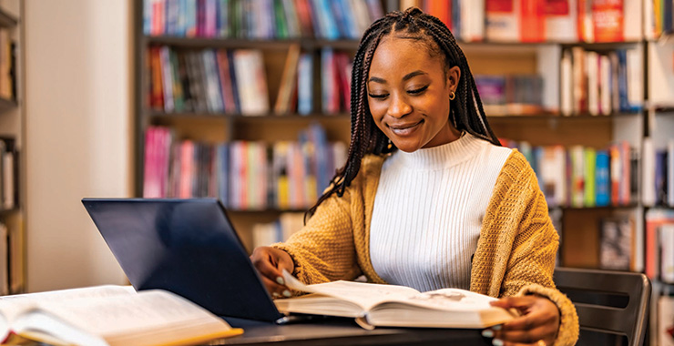 young woman reading a book at a table in a library