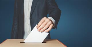 A person in a suit dropping a ballot into a box.