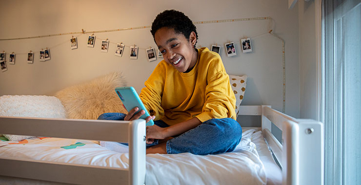 smiling teen boy scrolling through social media feed while sitting on his bed