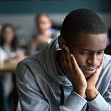 Young, African American man sits alone in cafe while others point and laugh behind him.