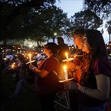 A large group of people attends a candlelight vigil, holding candles in remembrance