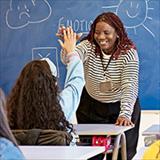 teacher and schoolgirl exchanging high-five in classroom