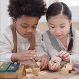 Two preschool students play with blocks together.