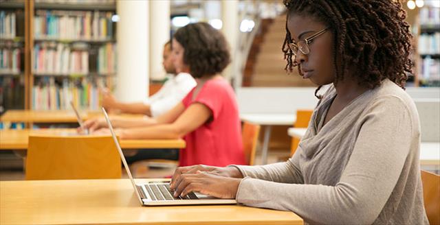 Adults working and researching individually at stations in a library with warm light