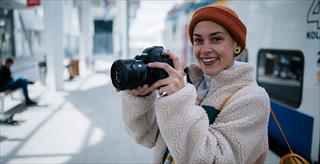 Young woman wearing an orange beanie holding a camera.