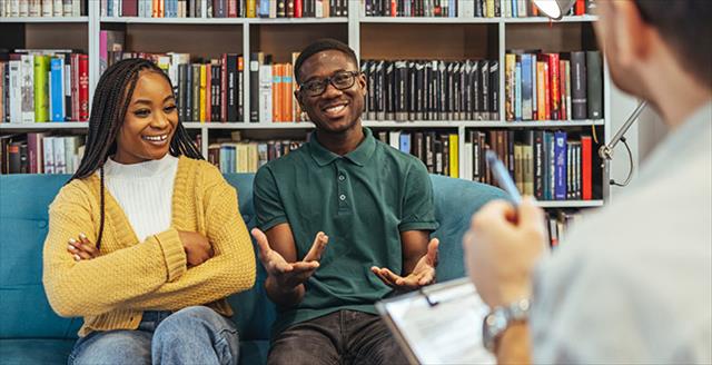 A young male-female couple talk together with a therapist in an in-person appointment