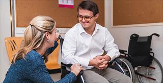 Therapist works with man in wheelchair who has Down syndrome.