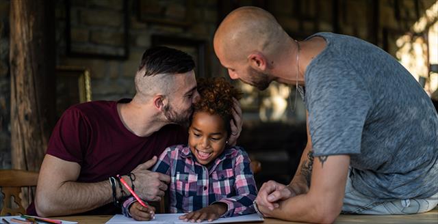 Same-sex couple coaching their child lovingly while she works on an assignment