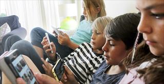 Children sitting together on a couch looking at their smart phones.