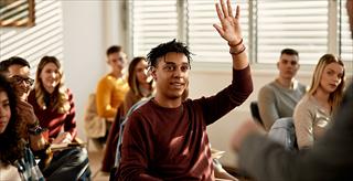 Male student raising his hand to ask a question in classroom.