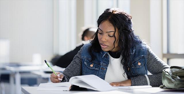 Student studying out of a book with intense concentration sitting in a brightly lit classroom