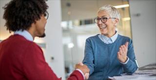 older White female manager shaking hands with younger Black male colleague