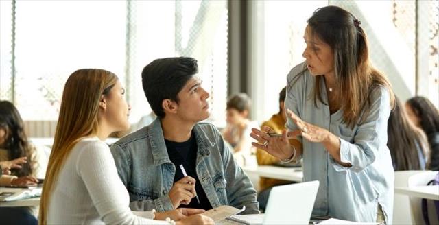 Teacher speaking with two students in a classroom.